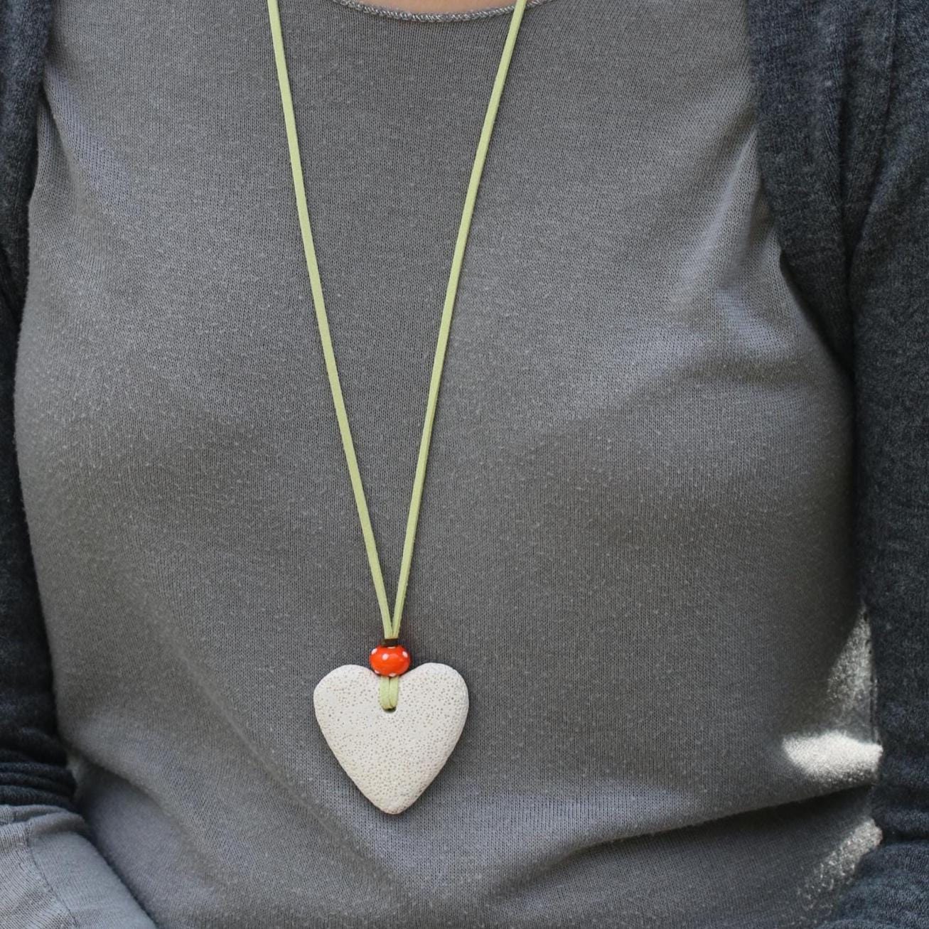 Handcrafted statement necklace with a white lava heart and orange bead, laid out on a neutral background to highlight textures and colors.