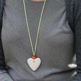 Handcrafted statement necklace with a white lava heart and orange bead, laid out on a neutral background to highlight textures and colors.