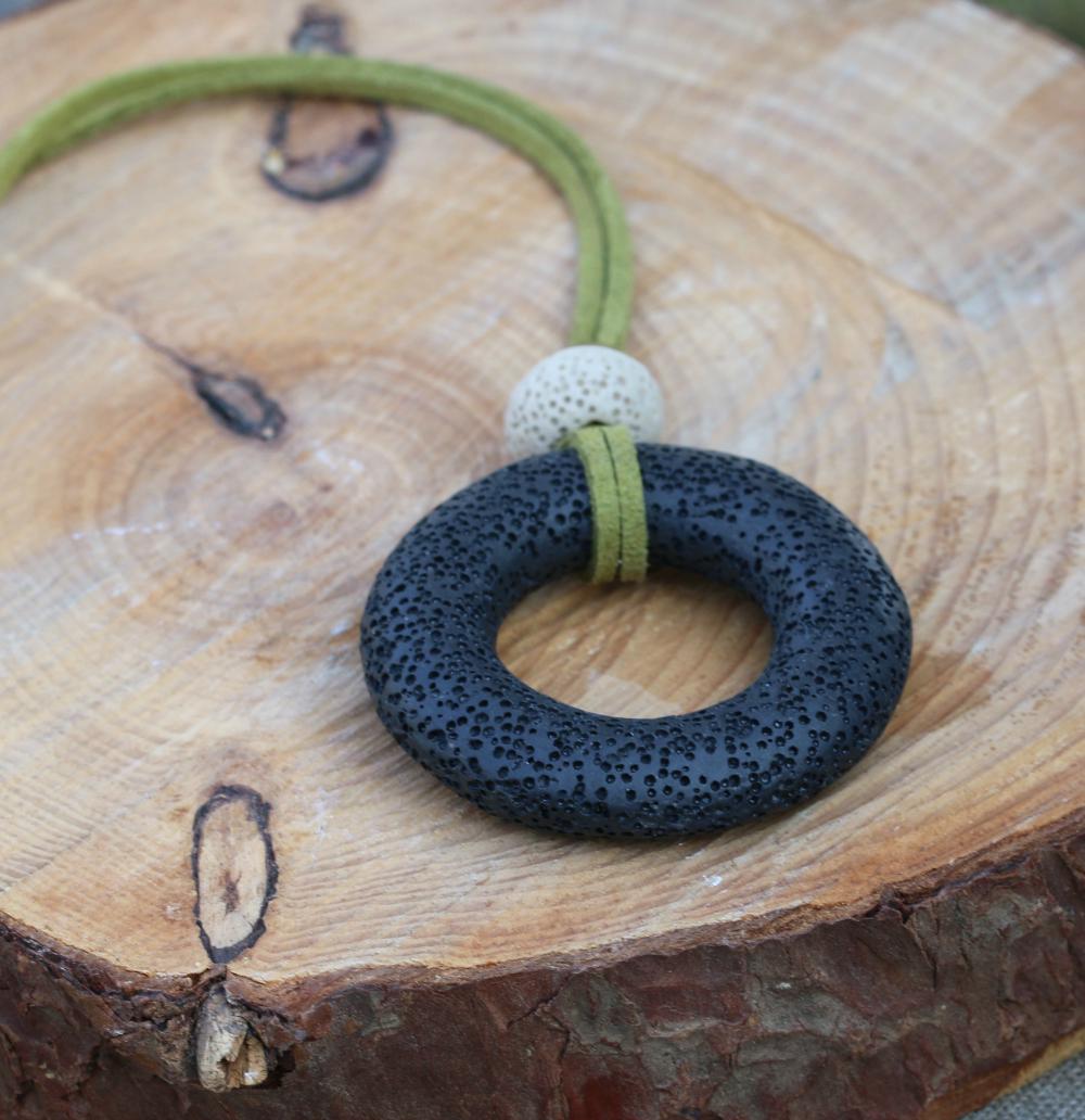 Handcrafted lava bead necklace with a single matte black volcanic stone pendant on an olive suede cord, laid flat to show detail.