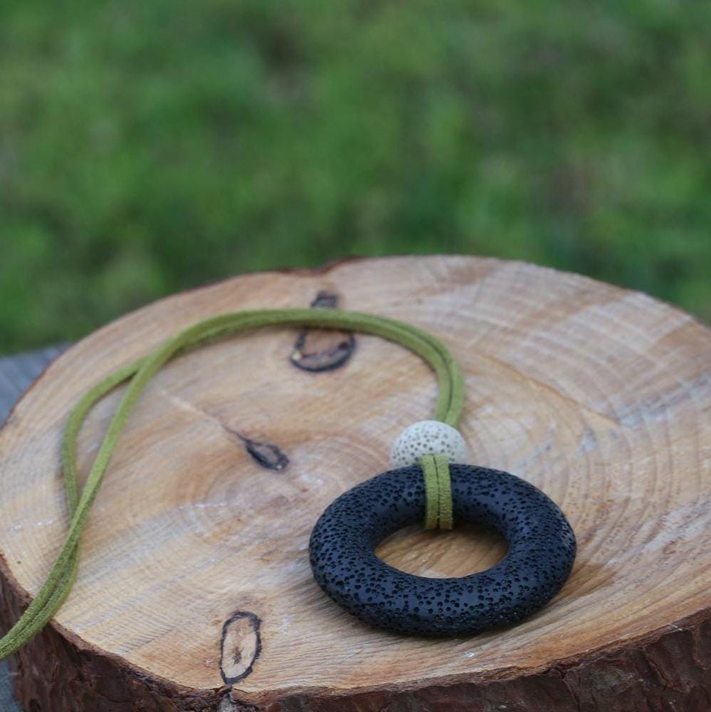 Artisan necklace with natural black lava rock bead and suede leather cord in green tones, styled as a minimalist, earthy accessory.