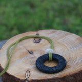Artisan necklace with natural black lava rock bead and suede leather cord in green tones, styled as a minimalist, earthy accessory.