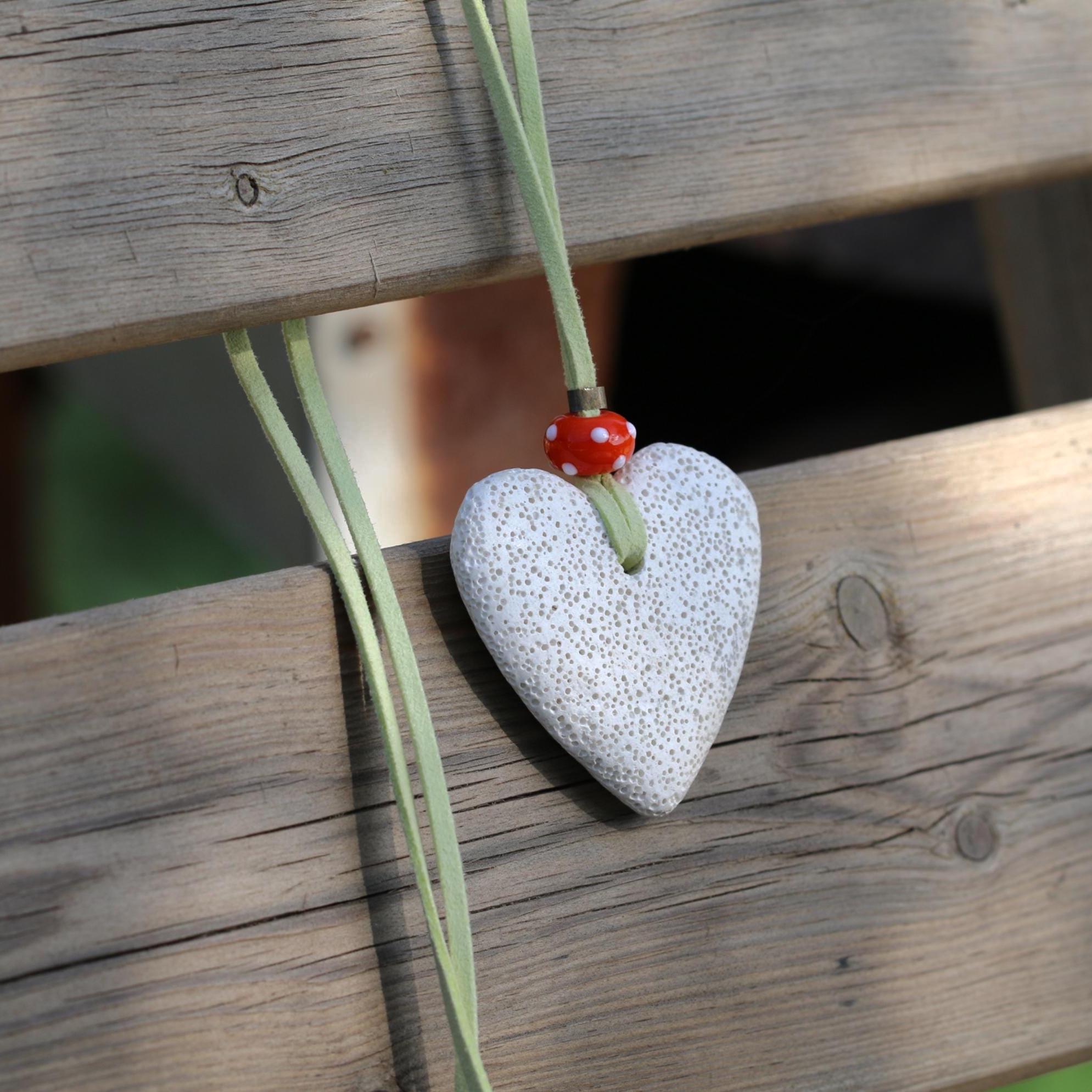 Long boho necklace with a white porous lava heart pendant and a bright orange glass bead, shown on a soft green suede leather cord.