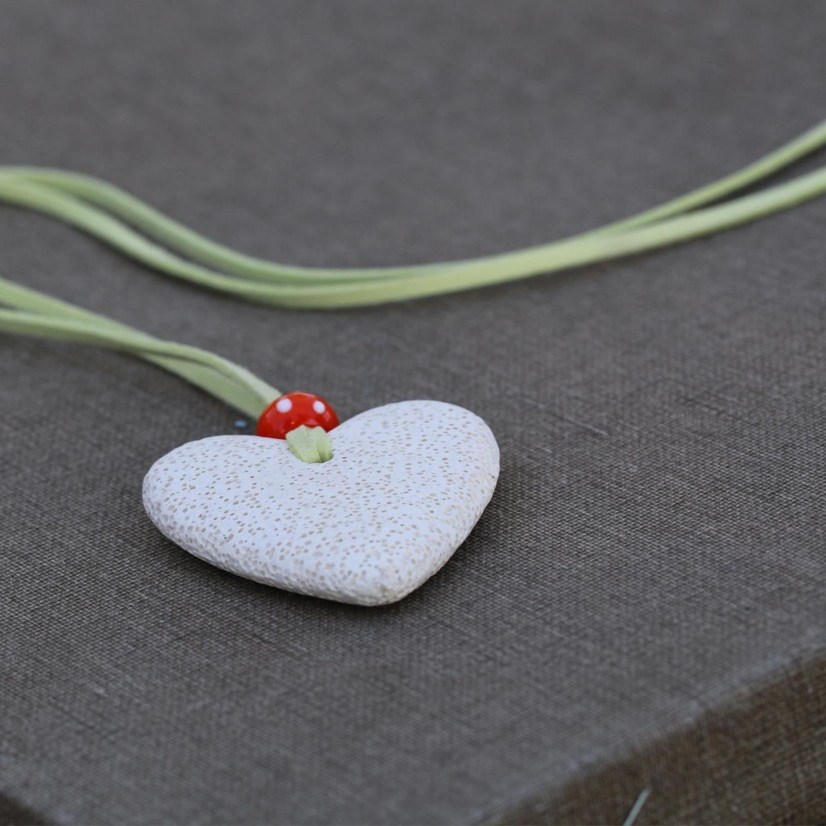 Nature-inspired handmade necklace with a chunky lava stone heart, colorful bead, and light green suede cord, displayed flat for full view.
