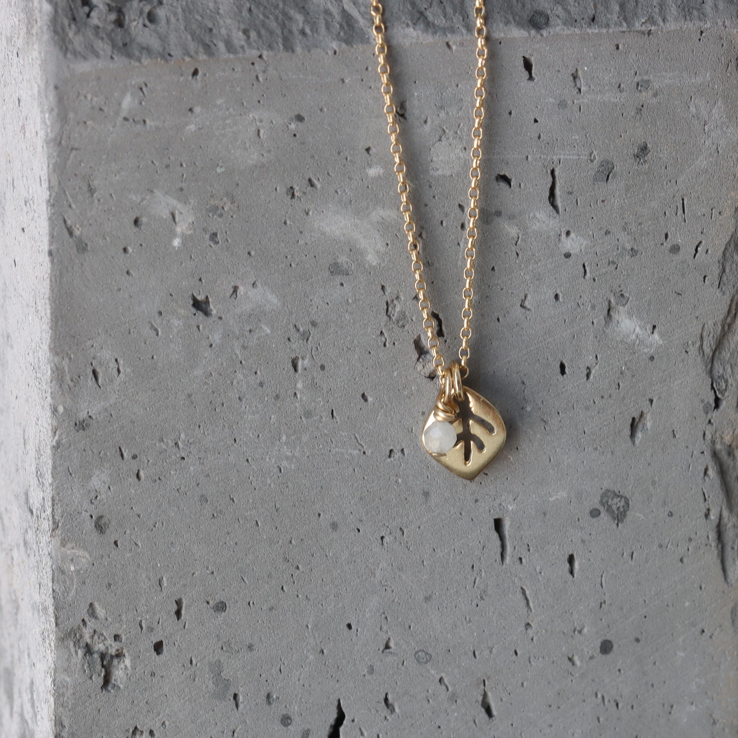 macro of the leaf pendant’s etched veins and polished edges with the moonstone charm catching light. The slim cable chain curves around the pendant; slate backdrop adds a natural, modern feel.