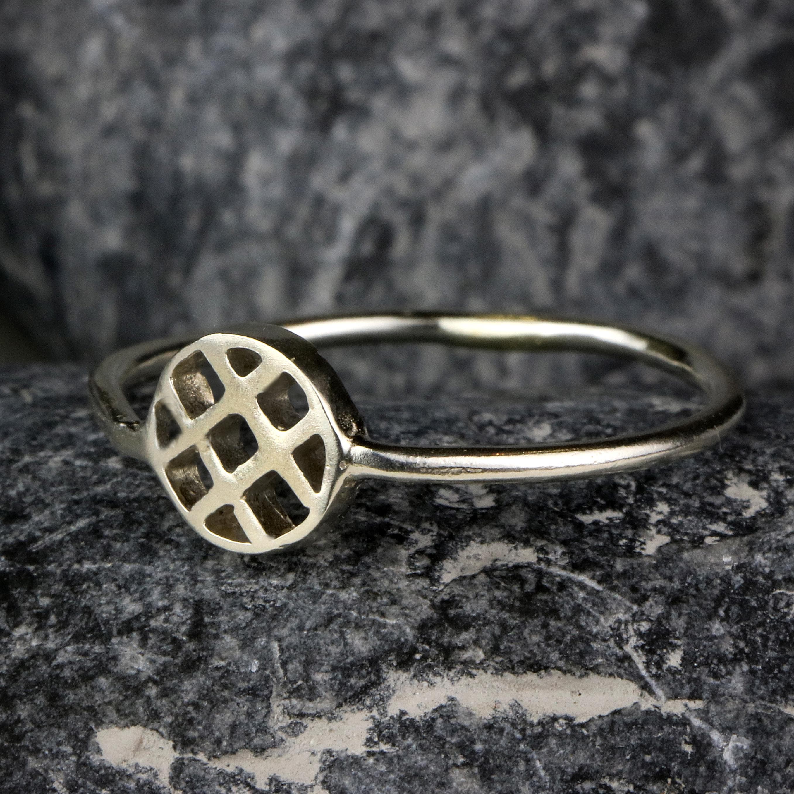 Close-up of a handmade silver lattice ring resting on gray stone. The open geometric circle top contrasts beautifully with the textured rock background, emphasizing the ring’s artisan finish.