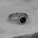 Modern minimalist silver ring with black faceted stone, photographed on neutral surface.