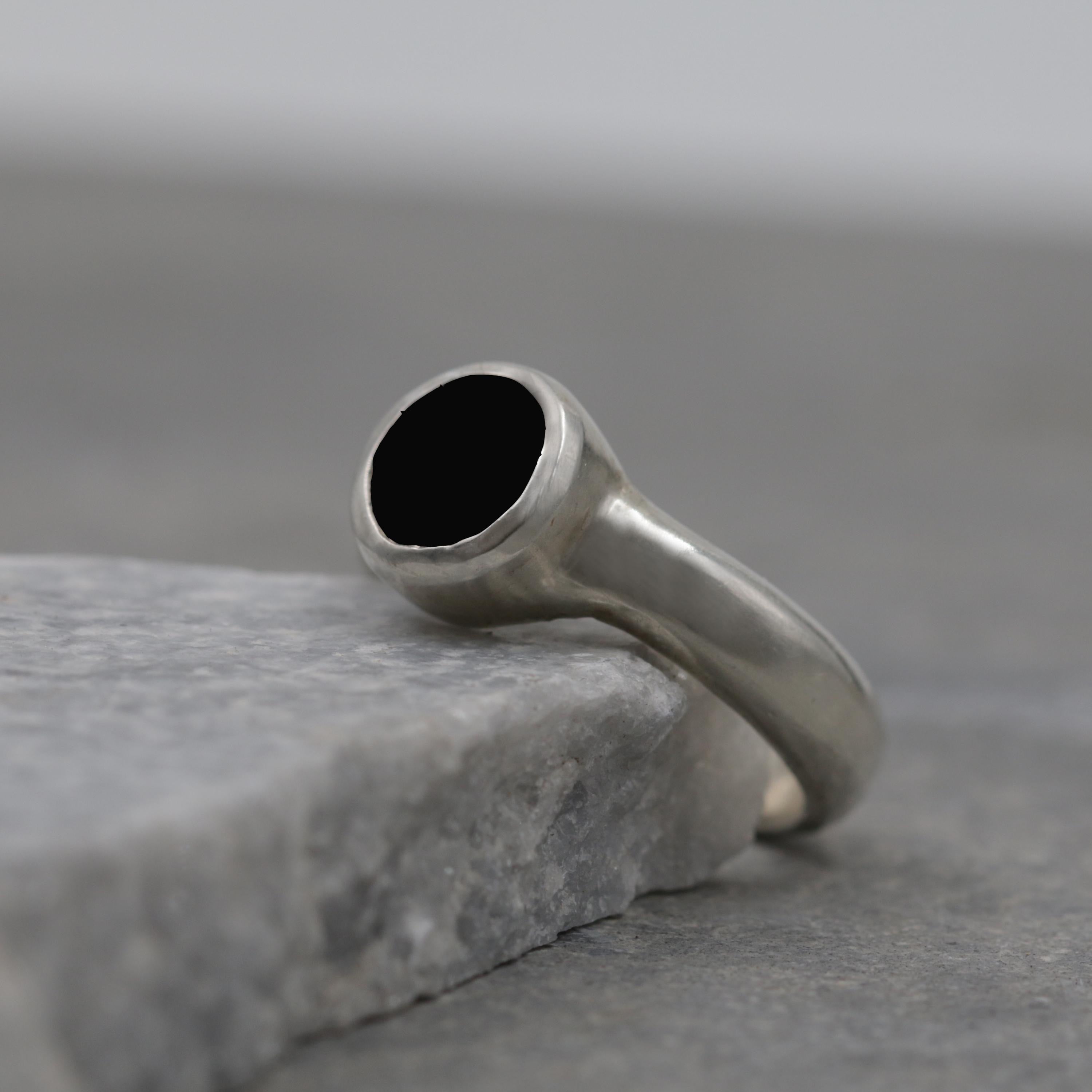 Handmade sterling silver solitaire ring with faceted black onyx gemstone on gray stone background.