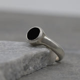 Handmade sterling silver solitaire ring with faceted black onyx gemstone on gray stone background.