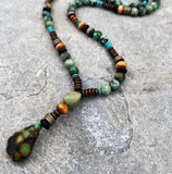 A long necklace made of turquoise, wood, and metal beads. The necklace has a large turquoise pendant at the end.