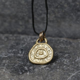 Unique handmade gold pendant with natural texture, coin-shaped and gently uneven. Inspired by organic forms found in nature, hanging on a fine wax cord.