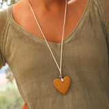 Long pendant necklace with a warm yellow lava heart, white suede leather cord, and artistic black and white bead, styled on a neutral background.