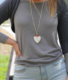 Bold pendant necklace featuring a heart-shaped white lava stone and orange glass bead, styled on a rustic green suede cord.