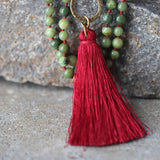 Side view showing the necklace draped on a display bust. Round green jade beads are evenly spaced on a burgundy waxed cord, finishing in a red-wine tassel. The long, over-the-head design emphasizes easy wear and a balanced, vertical line.
