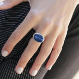 Model wearing the sterling silver kyanite set. The round pendant rests mid-chest on a delicate chain while the oval ring sits boldly on the index finger. The blue stones catch the light, showing natural bands and a polished cabochon surface for a refined look.