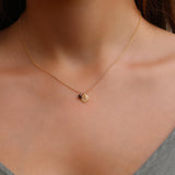 Detail shot of the leaf pendant showing engraved veins and a polished edge. A round garnet charm dangles beside the leaf, adding a pop of January birthstone red to the minimalist gold necklace.