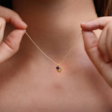 Model wearing a dainty gold leaf pendant with a petite garnet charm at the collarbone. The fine chain and small leaf silhouette create a subtle, feminine accent suitable for everyday wear or layering.