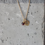 Macro image highlighting the pendant’s texture: fine leaf veins catch the light while a faceted garnet glows in deep crimson. The slim gold chain enhances the necklace’s delicate, nature-inspired design.
