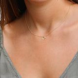 The dainty gold leaf pendant and small round moonstone hang centered on a fine chain. The moonstone shows a gentle flash; the leaf has satin texture. Clean neckline and neutral top emphasize the minimalist, nature-inspired design.