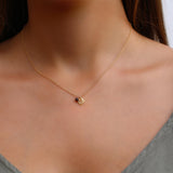 Semy Flat lay of a delicate gold leaf necklace paired with a tiny garnet gemstone charm. The rich red stone and warm gold tones are arranged in a gentle curve to highlight the pendant’s texture and light, airy feel.