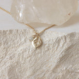 petite leaf with fine vein texture and a small round moonstone on a delicate chain. The pale stone backdrop brightens the gold and highlights the moonstone’s gentle adularescence.