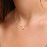 A woman wearing a delicate gold leaf pendant necklace with a tiny moonstone charm at the collarbone. The fine gold cable chain lays flat against the skin, highlighting the leaf’s subtle vein detail and the gem’s soft iridescent glow. Minimal, feminine, perfect for layering.