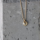 macro of the leaf pendant’s etched veins and polished edges with the moonstone charm catching light. The slim cable chain curves around the pendant; slate backdrop adds a natural, modern feel.