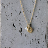Detail on gray stone: Close-up of the tiny moonstone and gold leaf pendant. Fine veins are visible on the leaf; the bezel-set moonstone shows iridescence. The gray stone backdrop gives a natural, earthy contrast to the polished gold.