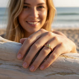 A gold starfish ring on a model’s fingers at the beach, capturing its ocean symbolism against sand, sea, and natural light