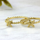 A delicate two gold starfish ring with a flat-dot band resting on a smooth white marble stone, highlighting its polished shine and ocean-inspired design