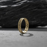 Gold geometric ring displayed on a smooth grey stone, showing the delicate cut-out design.
