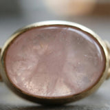 Close-up of the oval rose quartz ring highlighting the soft pink cabochon and polished gold bezel.
