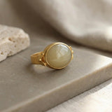 Front-facing view of the gold statement ring displaying the oval yellow gemstone and artisan finish layed on gray rock