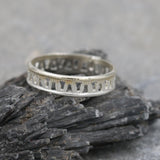Sterling silver geometric band photographed on a neutral surface with soft lighting.