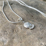Close-up of a sterling silver floral pendant necklace with a spiral bail, resting on a natural stone background.