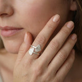 Close-up of a woman touching her cheek while wearing a sterling silver wrap ring with two textured leaf ends.