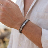 Man wearing a handmade sterling silver and leather bracelet with a geometric patterned silver centerpiece, styled with a white linen shirt.
