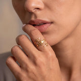 Woman wearing a gold spiral open wrap ring with delicate swirl and botanical details, shown in a close-up near her lips.