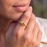 A close-up of a person's hand wearing a gold ring with a yellow gemstone.