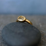 A gold ring with a yellow gemstone sits atop a gray rock.