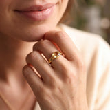 A close-up of a person's hand wearing a gold ring with a yellow gemstone.