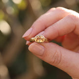 A close-up image of a person's hand holding a gold ring with a yellow gemstone, possibly an amber or amber-colored gemstone.