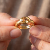A close-up image of a person's hands holding a gold ring with a large gemstone in the center.