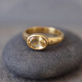 A gold ring with a yellow gemstone, possibly a citrine, sits on a gray rock.