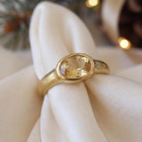 A gold ring with a large oval-shaped gemstone is displayed on a white napkin.