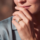A close-up of a person's hand wearing a gold ring, with their hand resting on their chin.