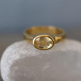 A gold ring with a yellow gemstone, possibly a citrine, is displayed against a blurred blue background.