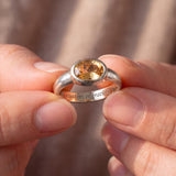 A close-up image of a person's hands holding a silver ring with a large, clear gemstone in the center.